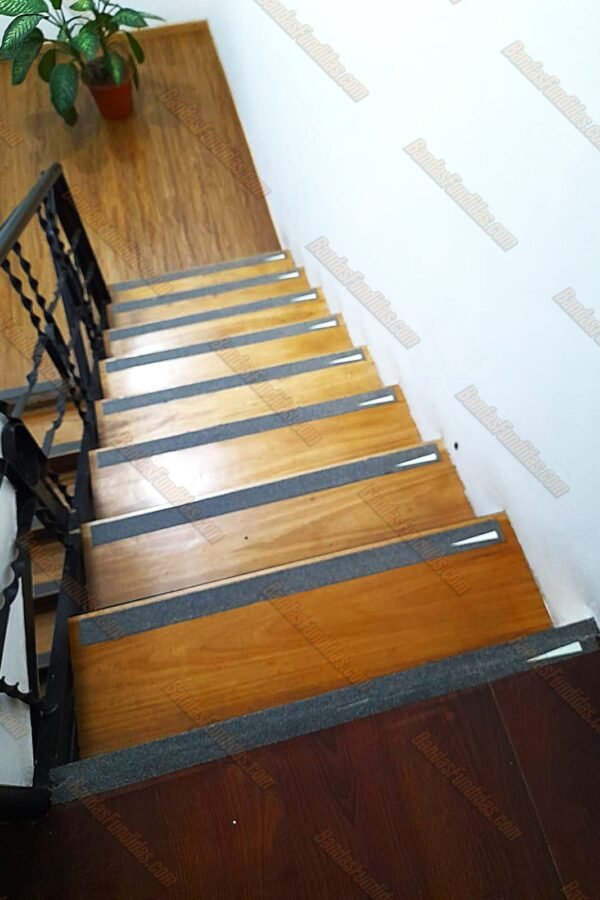 Bandas antideslizantes fundidas con línea fotoluminiscente aplicadas sobre escaleras interiores tipo madera para visibilidad nocturna.