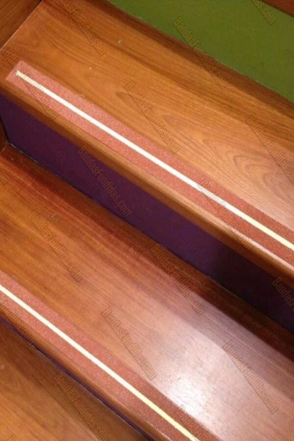 Bandas fundidas antideslizantes con línea fotoluminiscente aplicadas sobre escaleras interiores tipo madera para visibilidad nocturna.
