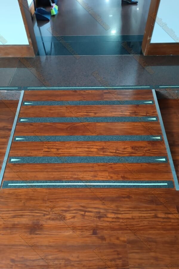 Bandas antideslizantes fundidas con línea fotoluminiscente y ojo de gato lateral aplicadas sobre rampas interiores tipo madera para visibilidad nocturna