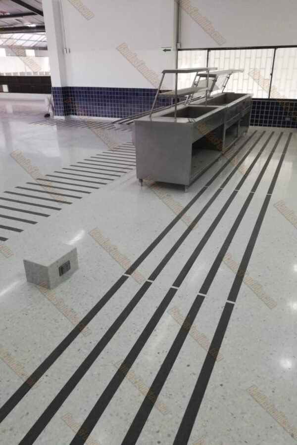 Bandas antideslizantes fundidas instaladas en piso liso de zona de servicio y tráfico peatonal en cafetería para protección de usuarios.