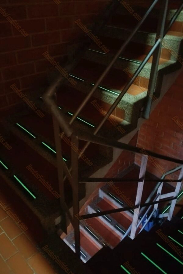 Bandas antideslizantes fundidas con tecnología fotoluminiscente activándose en escaleras en curva estilo caracol en baldosín con poca iluminación para prevenir caídas.